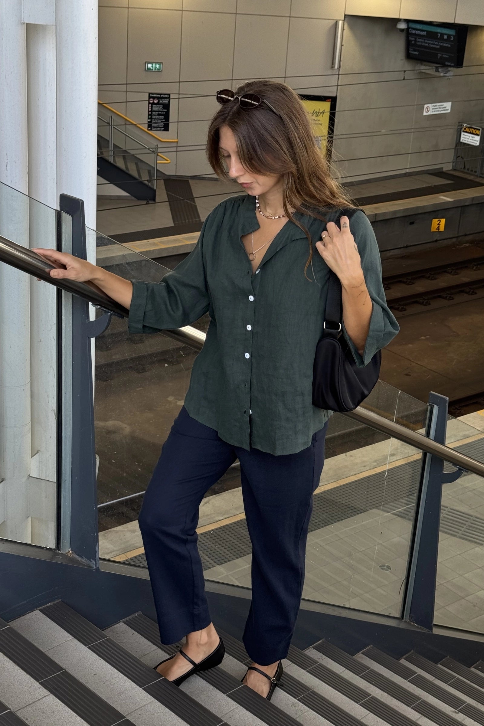 Woman in a green shirt and navy pants standing on a subway platform.