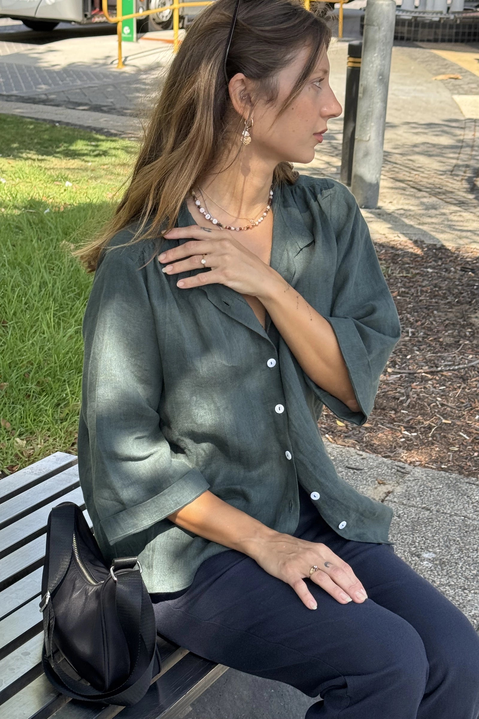 Woman sitting on a bench wearing a green shirt and dark pants, with a black bag beside her.