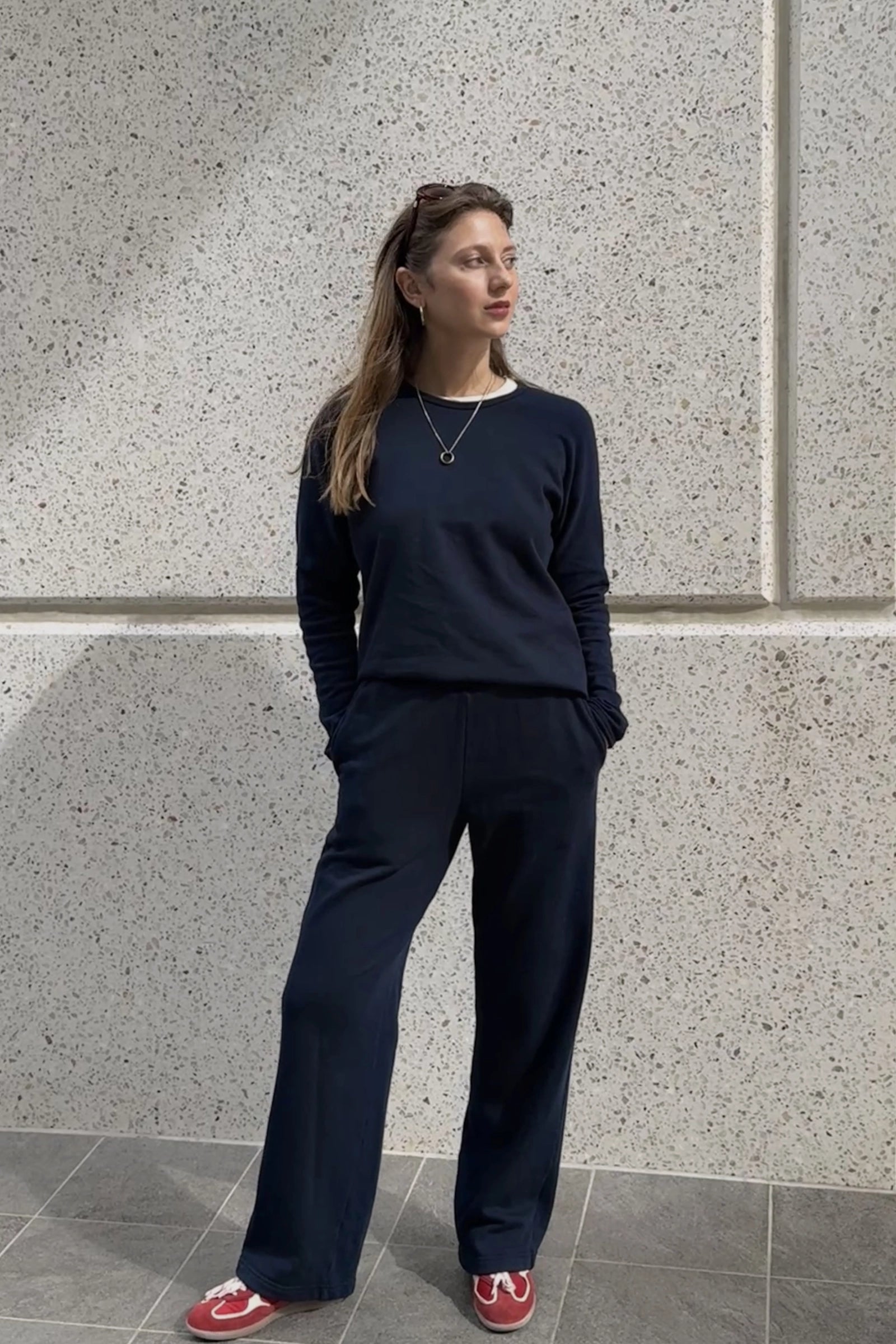 Woman wearing a navy outfit standing against a textured wall.
