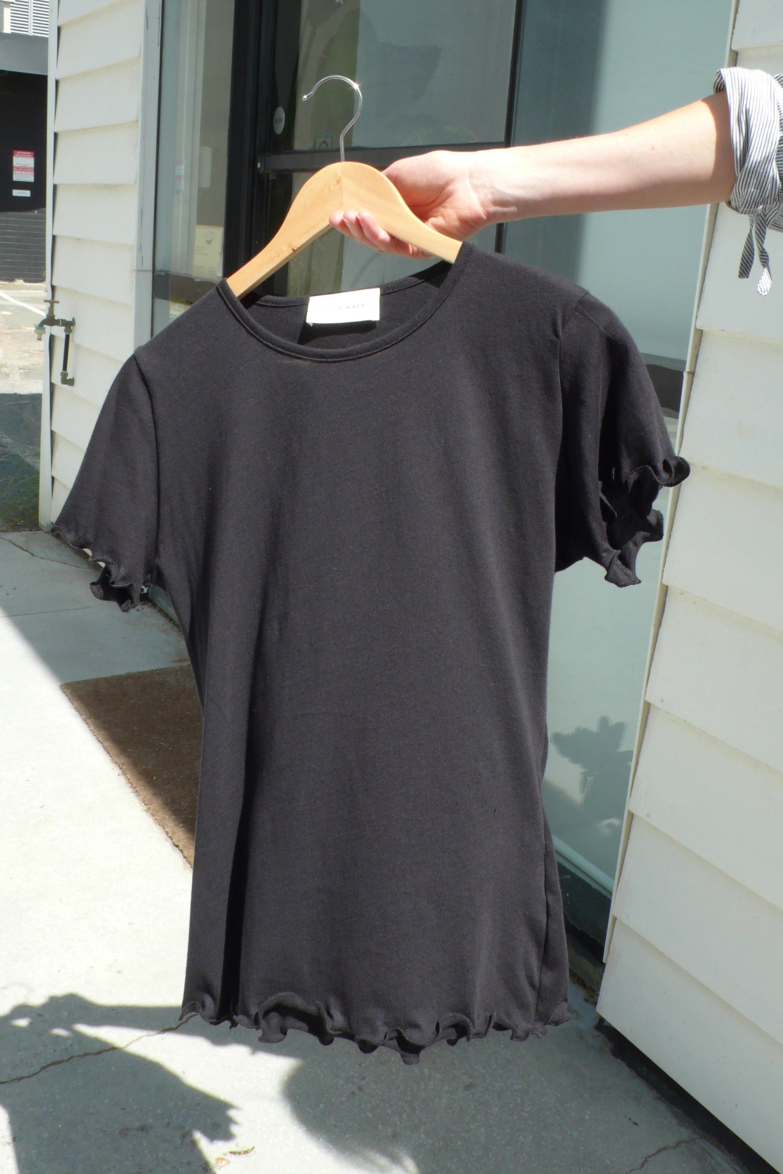 Black t-shirt on a hanger held by a person outdoors.
