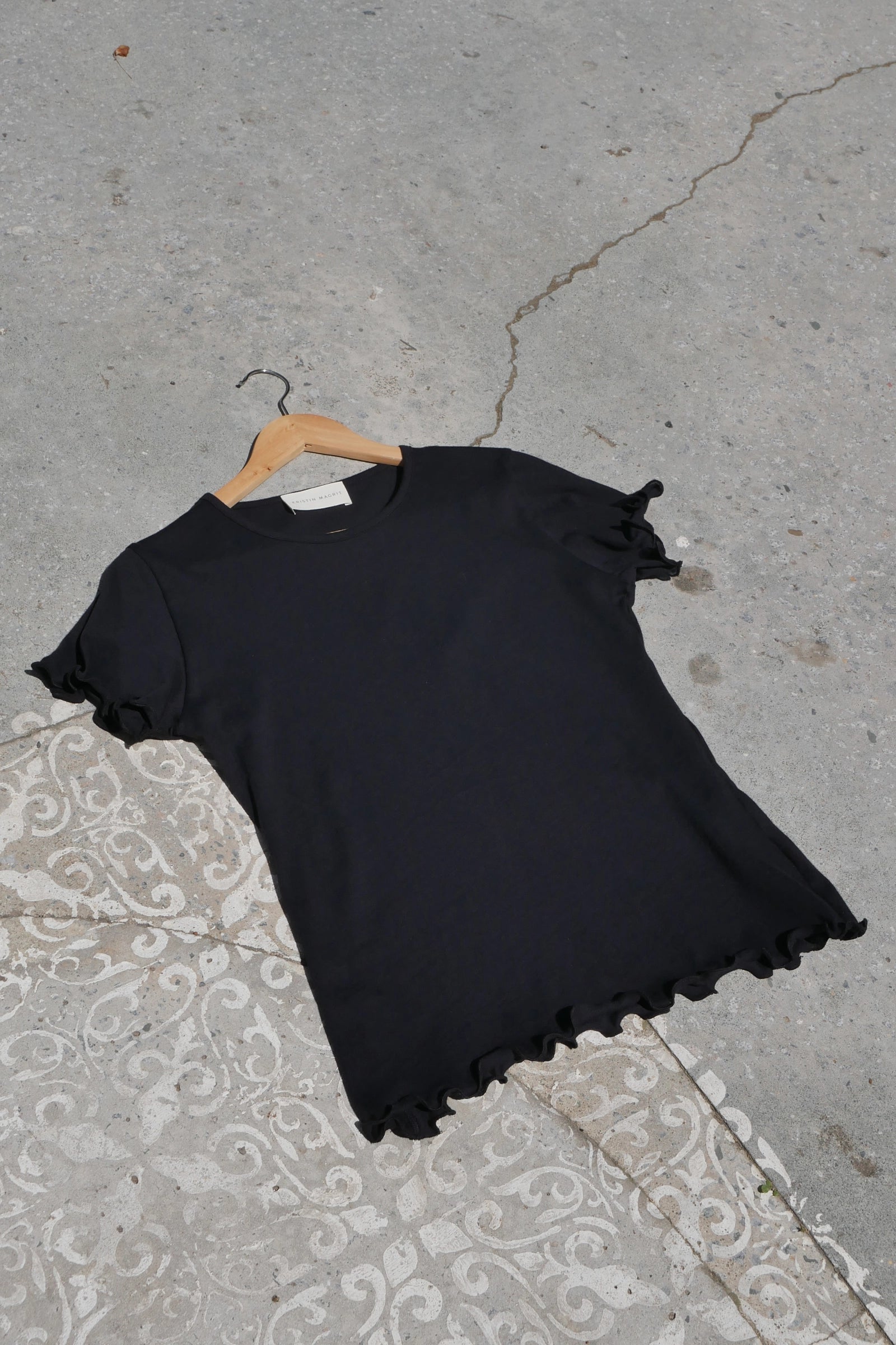 Black ruffled tshirt on a hanger against a concrete background