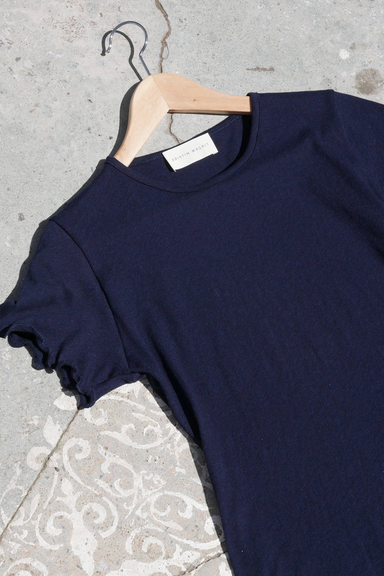 Navy blue t-shirt on a hanger against a textured concrete floor.