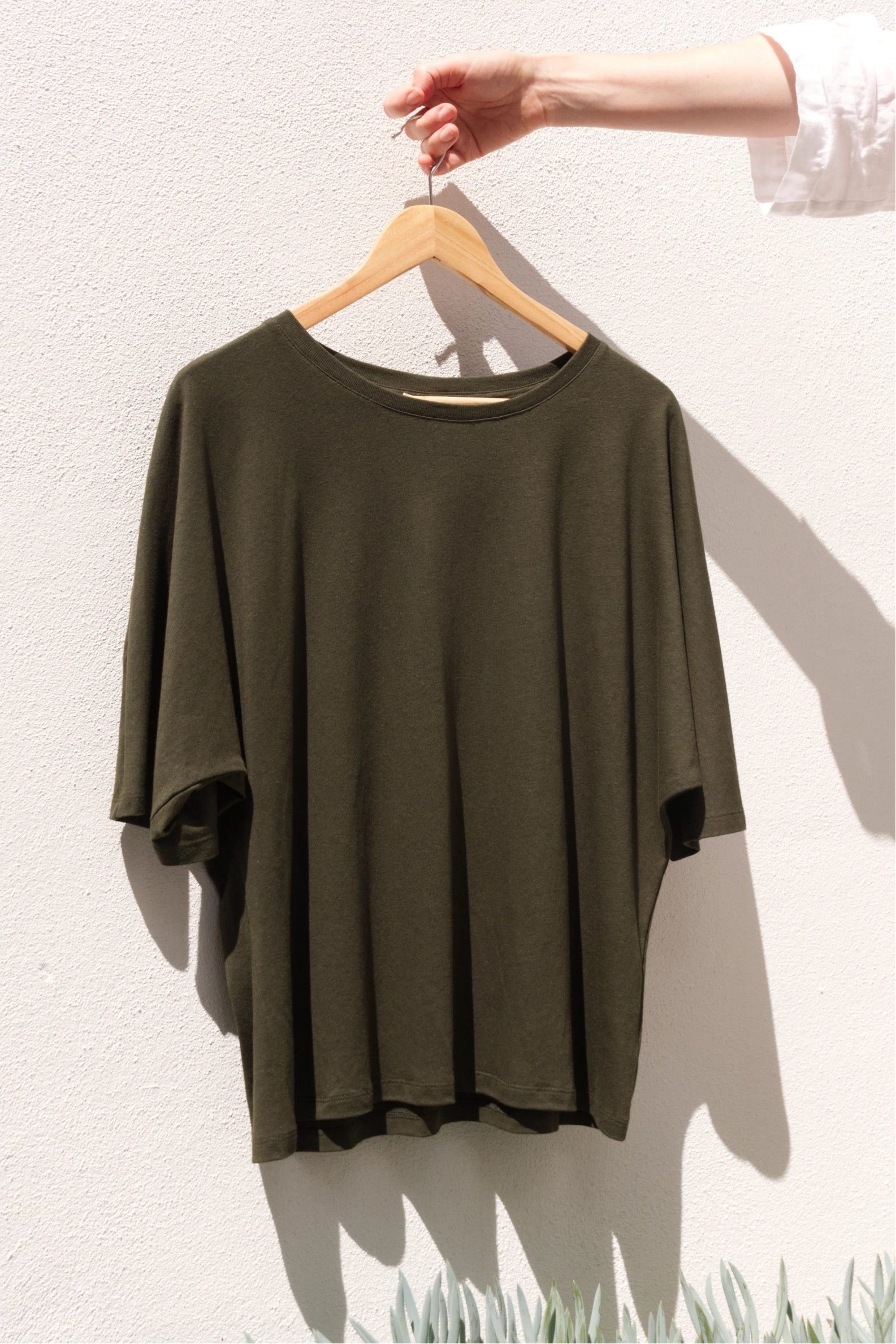 Green Tshirt on a hanger against a white wall