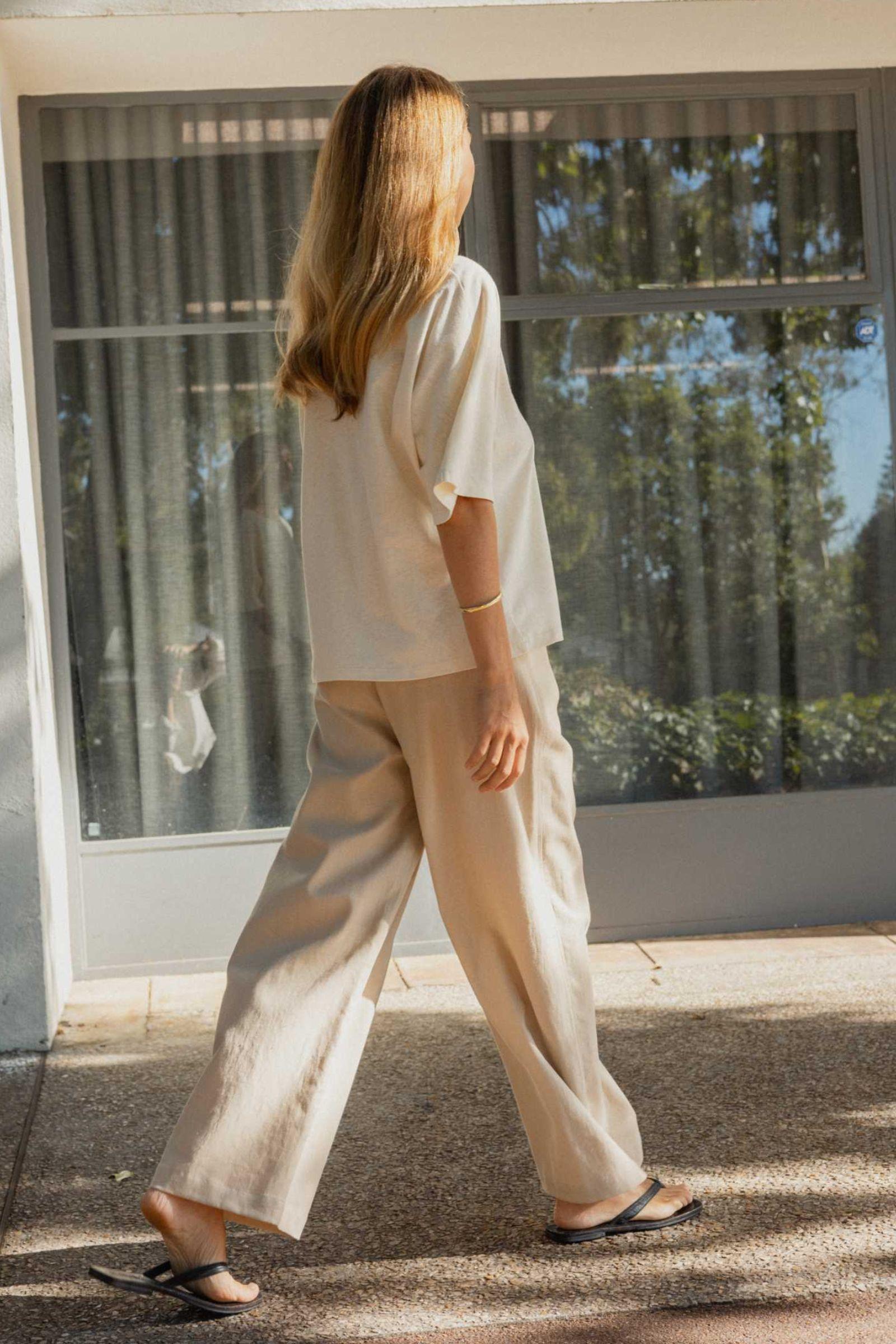 Woman walking outdoors wearing a cream top and beige pants.