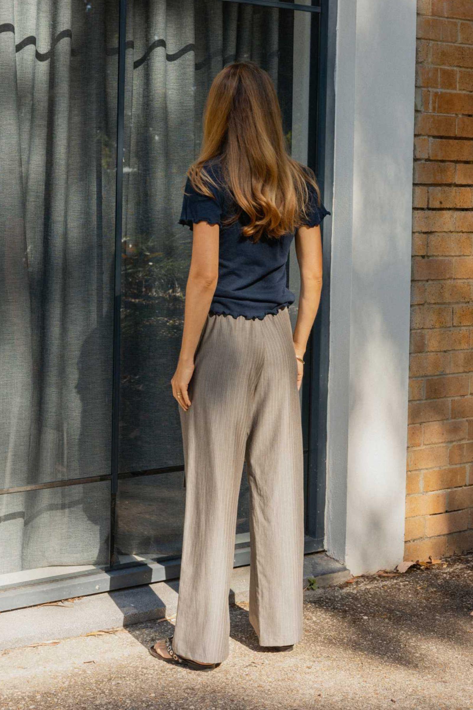 Woman wearing a navy top and grey pants standing in front of a glass door.