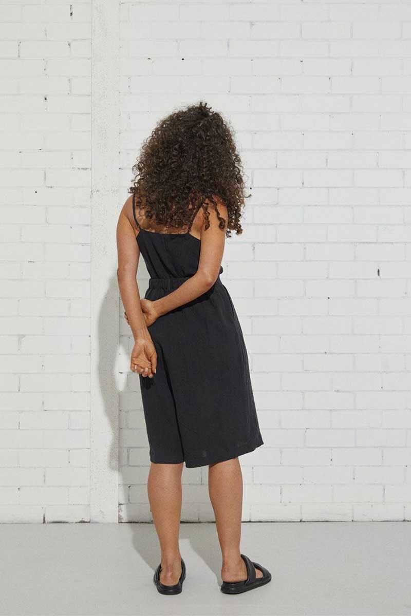 kristin magrit sailor long shorts are short finishing at the knee, a longer length short, colour black organic linen, Buttons made from sustainable coconut shell, model standing in studio black top back view