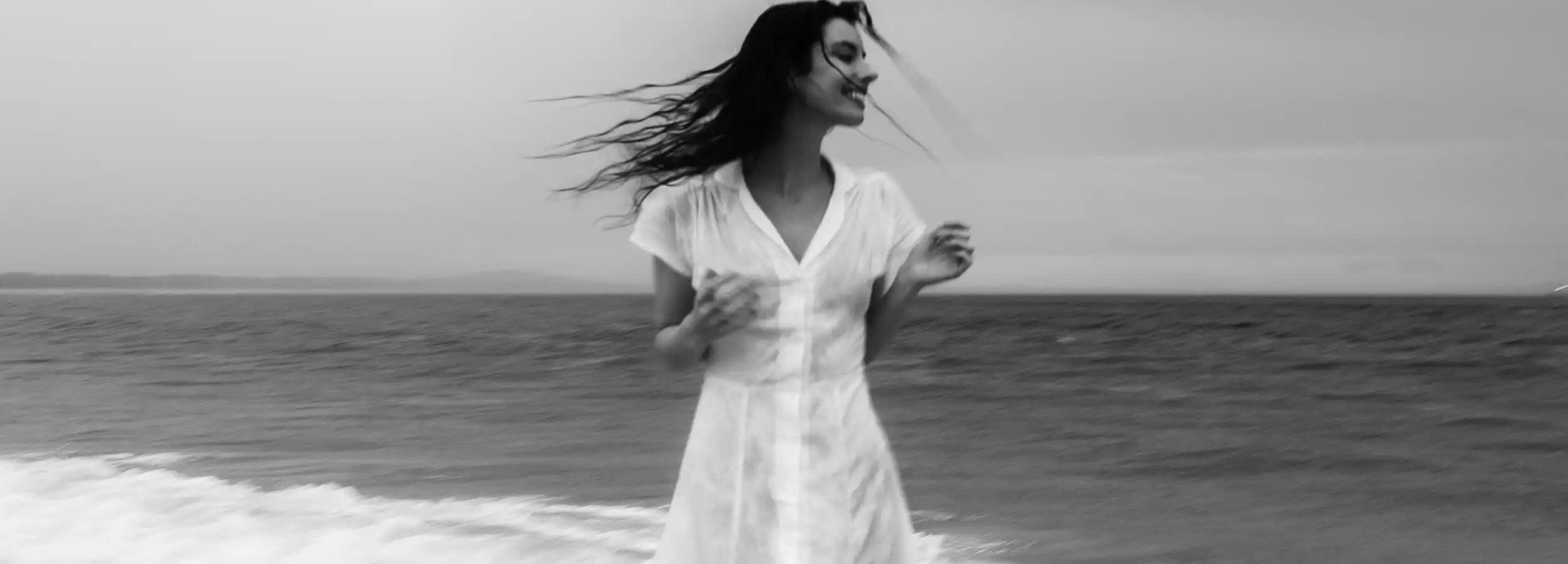 black and white image of model in white linen Kristin Margit dress Indian ocean in back ground 