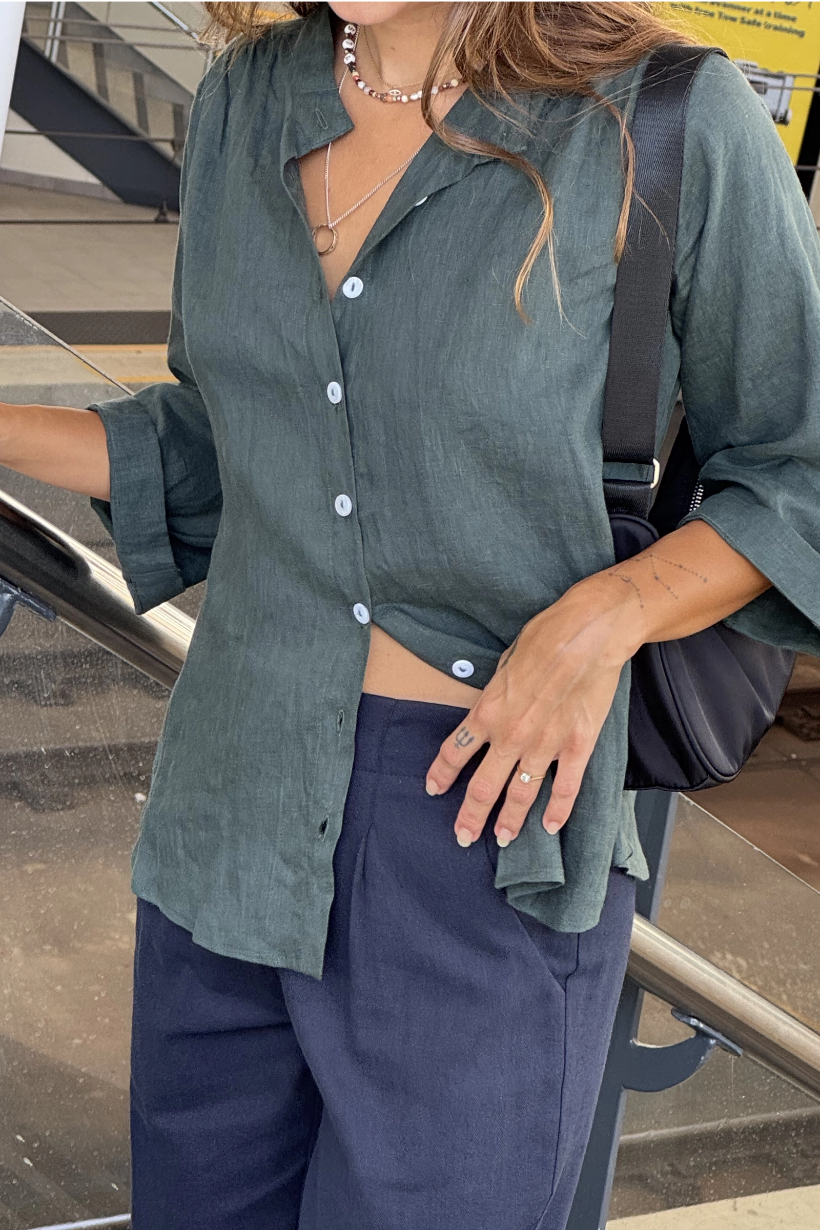Person wearing a green shirt and blue pants with a handbag, standing on a staircase.
