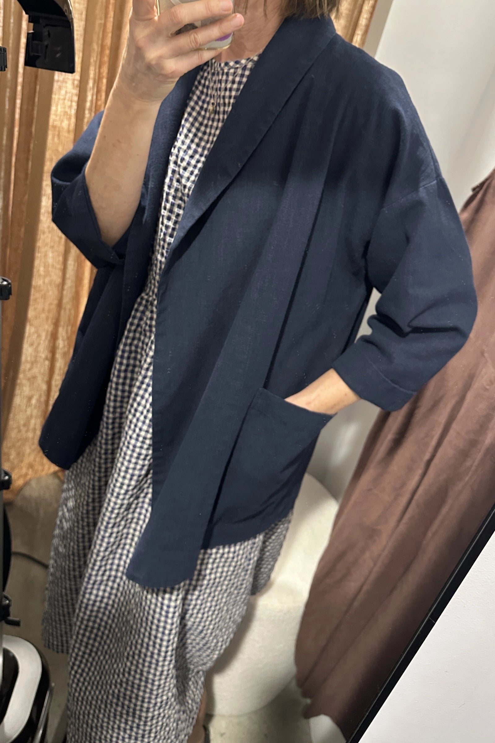 Person wearing a navy blazer over a checkered dress in a neutral setting