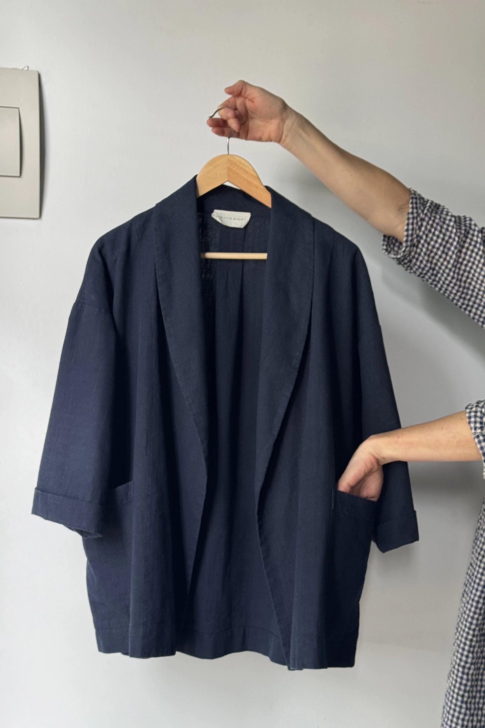 Navy blue coat on a hanger held by a person against a white wall