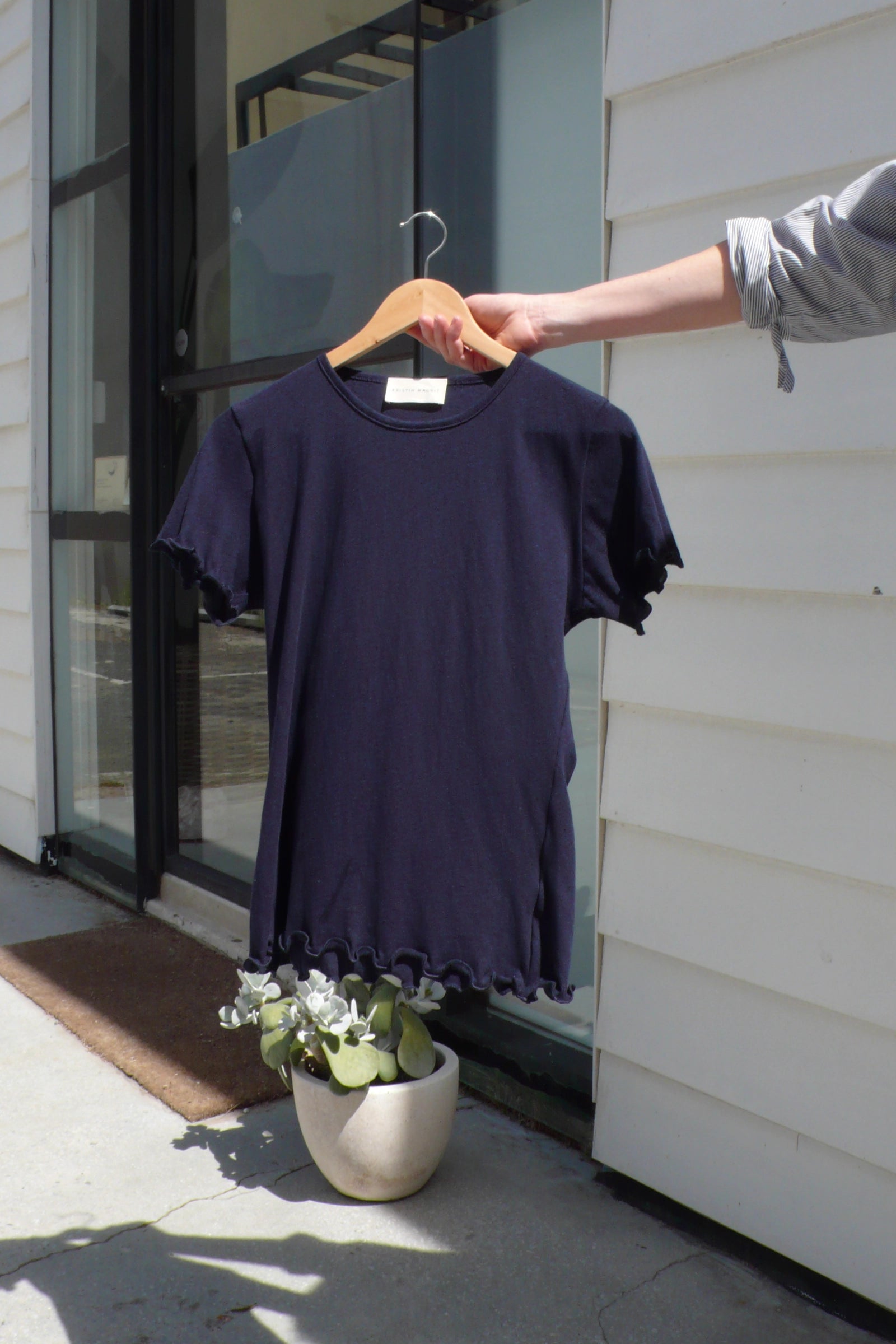 Navy blue tshirt on a hanger held by a person outside a building.