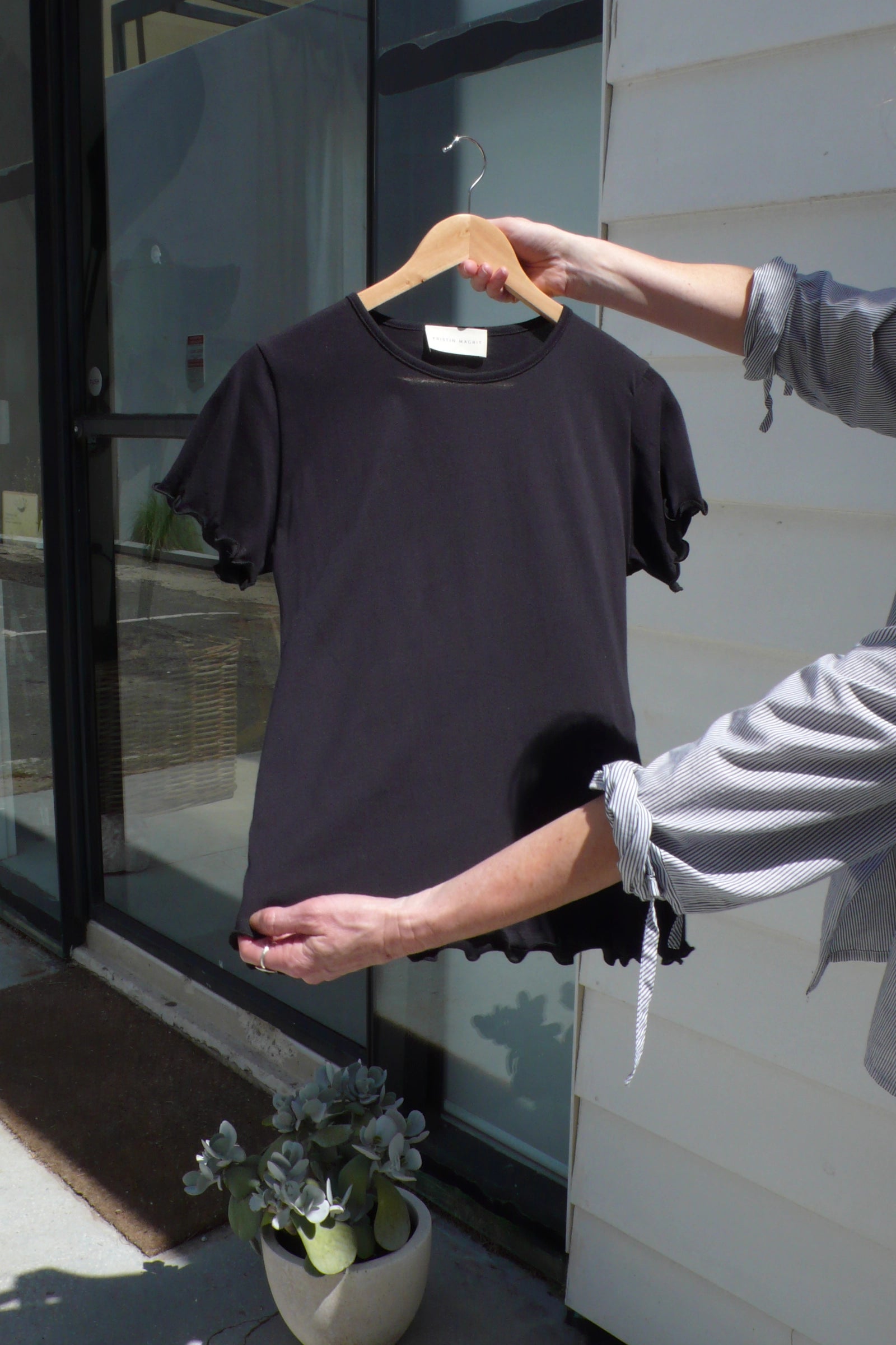 Black t-shirt on a hanger held by a person outdoors.
