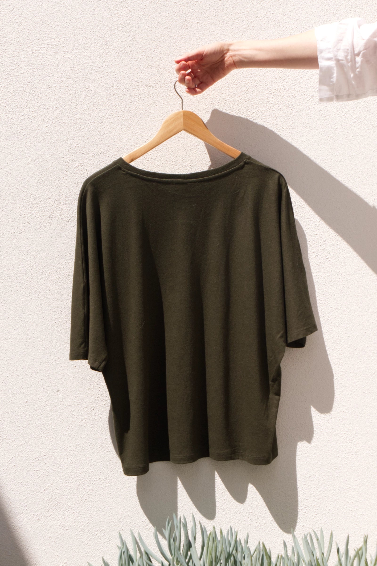 Olive Top on a hanger against a white wall