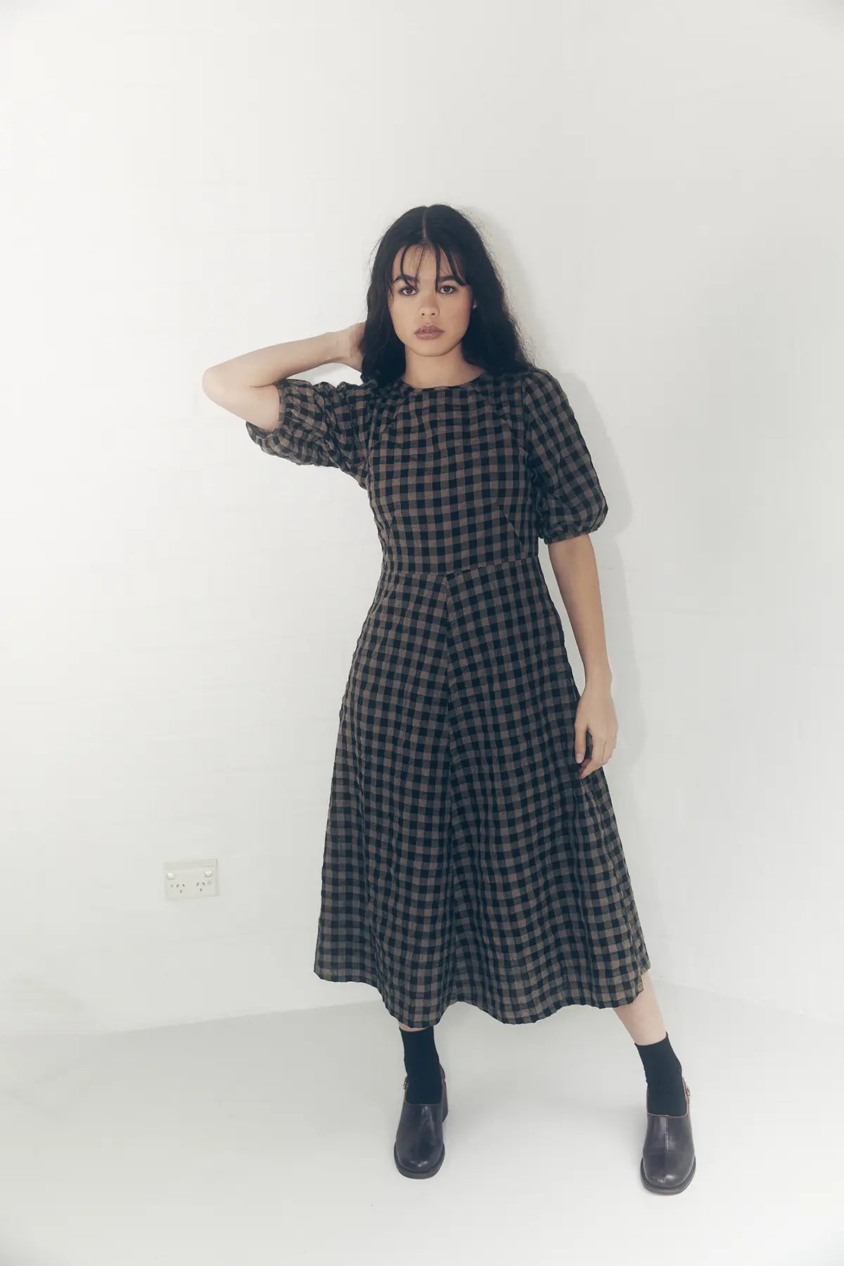 model standing hand on head in a line gingham dress colour mocha and black