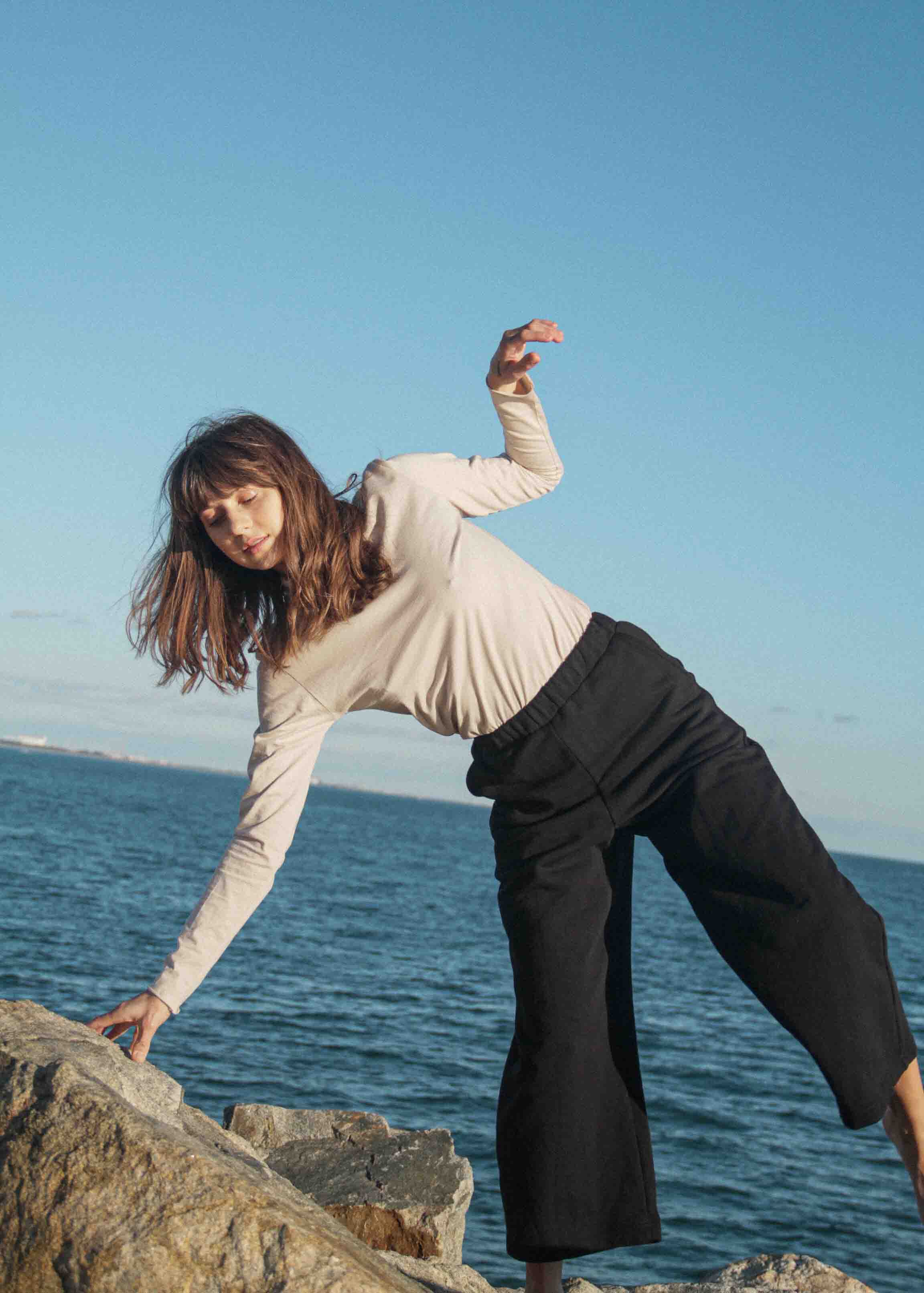 Girl is climbing over rocks wearing sand cotton skivvy and organic cotton wide legged tracksuit trousers.